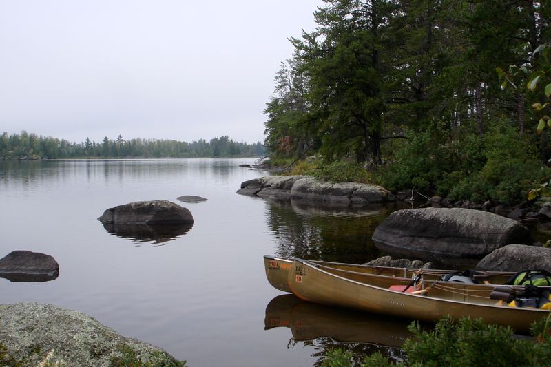 Canoes pulled up on a rocky shore of a calm, pine-lined lake in the Boundary Waters